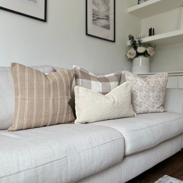 set of 3 square cushions, one oatmeal colour with vertical white stripes, 1 cream and brown large squares and 1 cream with small beige floral print and 1 rectangle cushions with a cream boucle texture