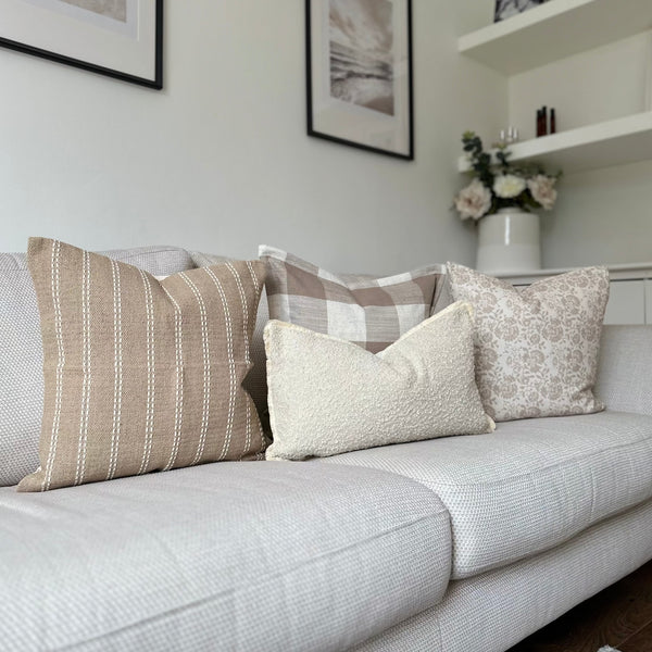 set of 3 square cushions, one oatmeal colour with vertical white stripes, 1 cream and brown large squares and 1 cream with small beige floral print and 1 rectangle cushions with a cream boucle texture