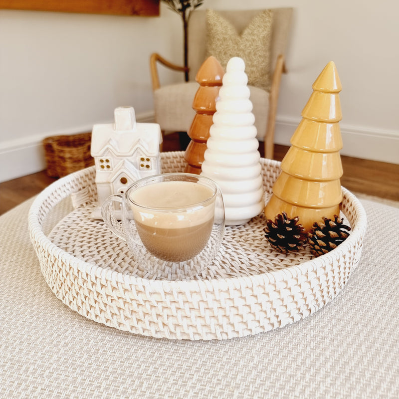 round white wash rattan tray with cut out handles either side. Styled on a cream surface with a glass mug filled with coffee and autumn decorative ornaments