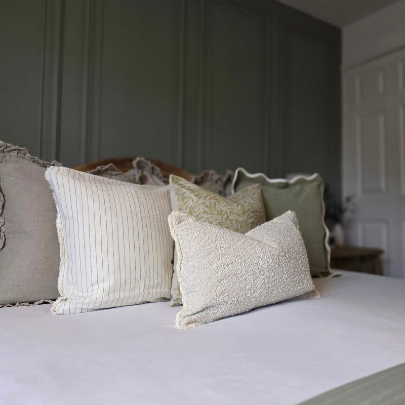 A cushion set of 3 square and 1 rectangle cushions with a mixture of green and cream plain and leaf prints to create a serene look on a bed with white bedding