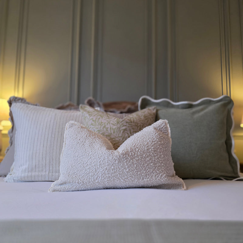 A cushion set of 3 square and 1 rectangle cushions with a mixture of green and cream plain and leaf prints to create a serene look on a bed with white bedding