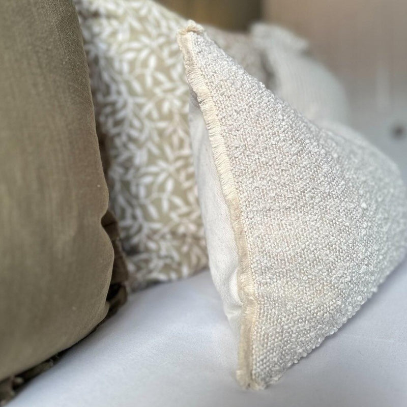 CLOSE UP OF THE SIDE OF THE CREAM BOUCLE RECTANGLE , CUSHION, with a cream fringed edge