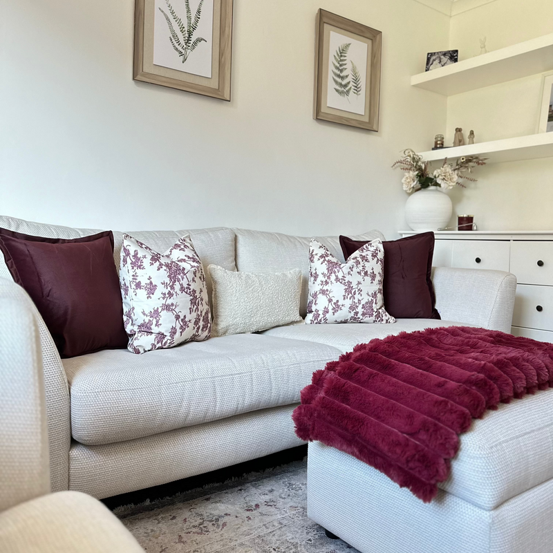 Set of 5 cushions. 2 x square velvet burgundy cushions, 2 x square cream cushions with a burgundy floral print and 1 x rectangle cream boucle cushion. All sat on a cream sofa