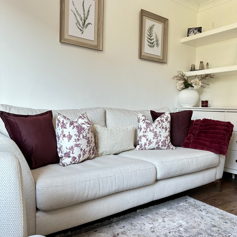 Set of 5 cushions. 2 x square velvet burgundy cushions, 2 x square cream cushions with a burgundy floral print and 1 x rectangle cream boucle cushion. All sat on a cream sofa