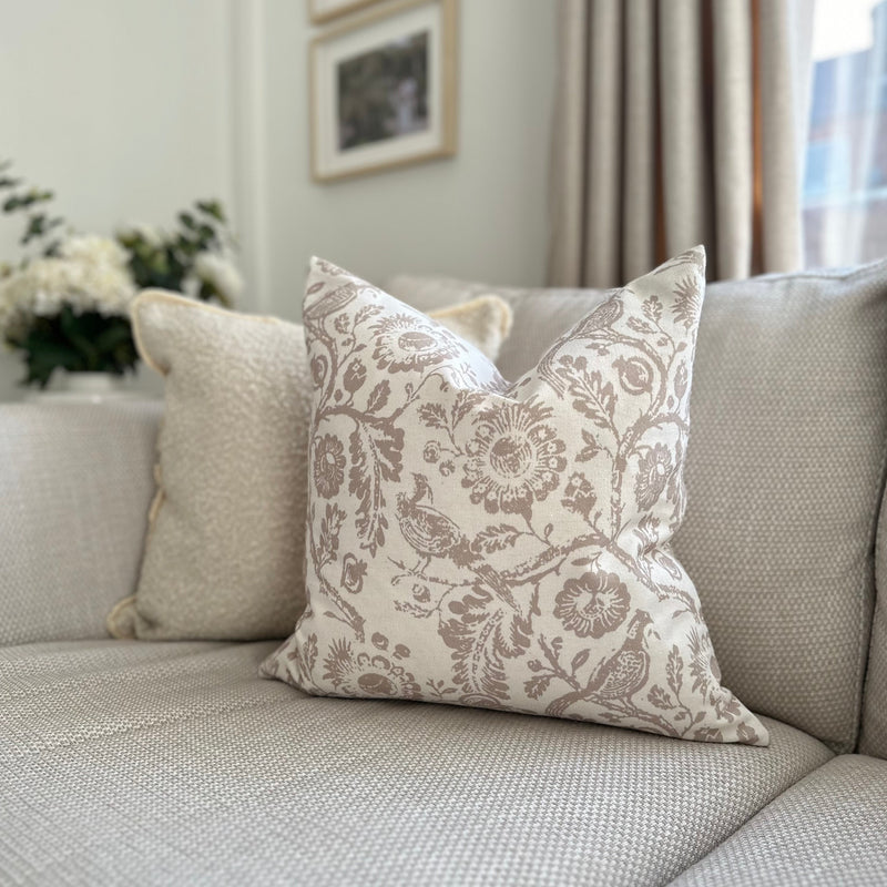 square cream cushion with a large beige floral and bird print. Sat on a cream living room sofa