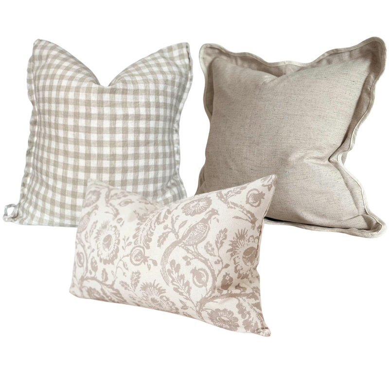 A set of 3 cushions. 1 square linen cream cushion with an all over beige gingham print and weathered edges. 1 square cotton greige cushion with a scalloped cream coloured edge. Rectangle cotton cream cushion with a large brown floral and pheasant bird print. All on a white back ground for contrast