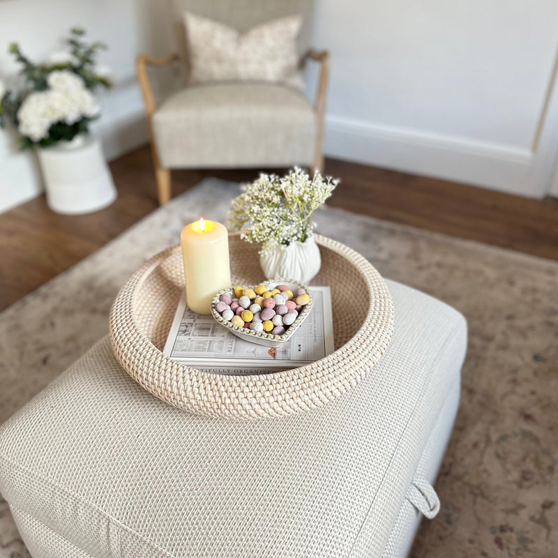 White wash Round Rattan Tray with candle, heart bowl filled with mini eggs and a white vase inside. All sat on a cream footstool