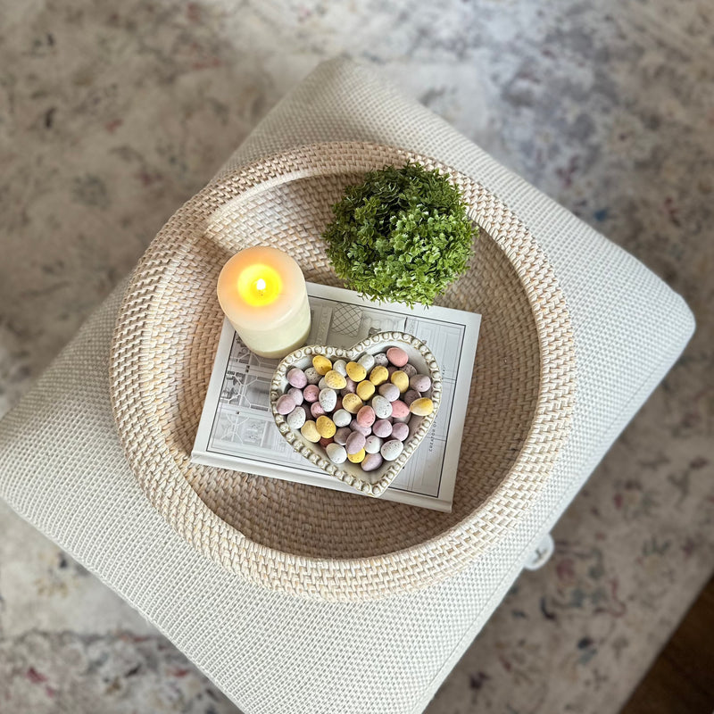 Birds eye view of large white wash round rattan tray filled with heart shape bowl, faux hebe bush and a candle