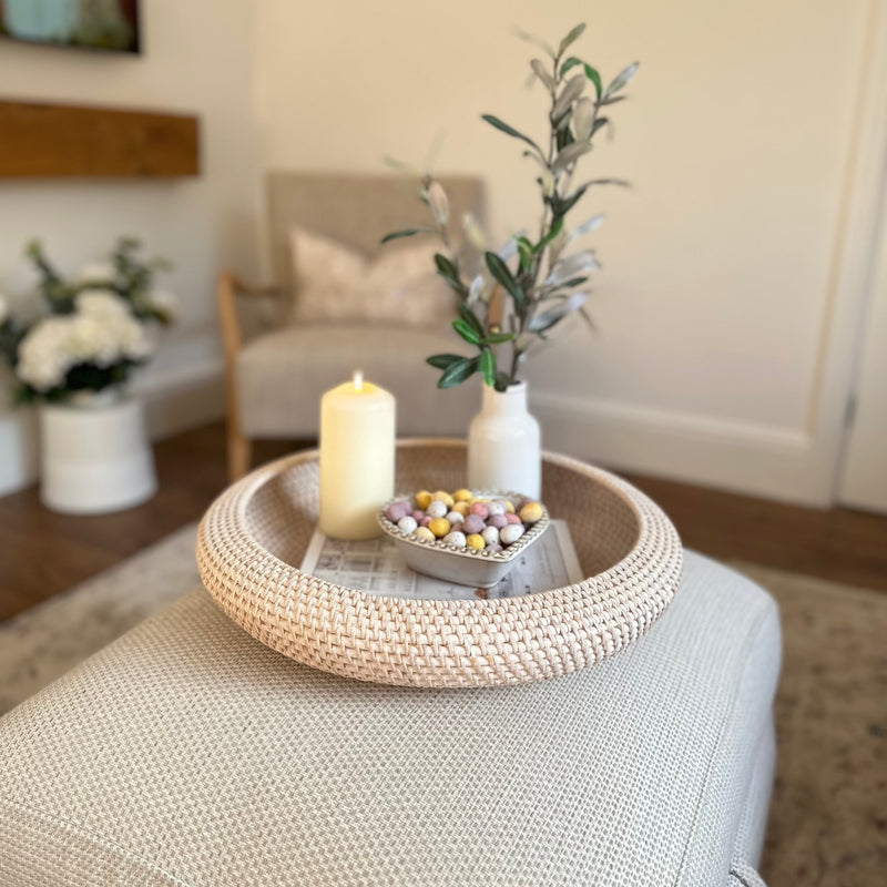 White wash Round Rattan Tray with candle, heart bowl filled with mini eggs and a white vase inside. All sat on a cream footstool