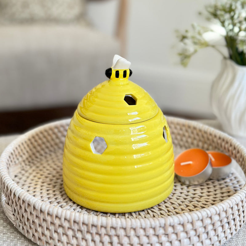 Ceramic yellow beehive shaped oil and wax burner with bumble bee in lid. All sat on a rattan round white tray
