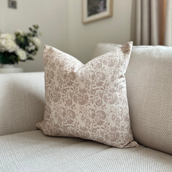 square cream cushion with a delicate taupe/beige floral pattern motif all over front and back. Sat on a cream sofa