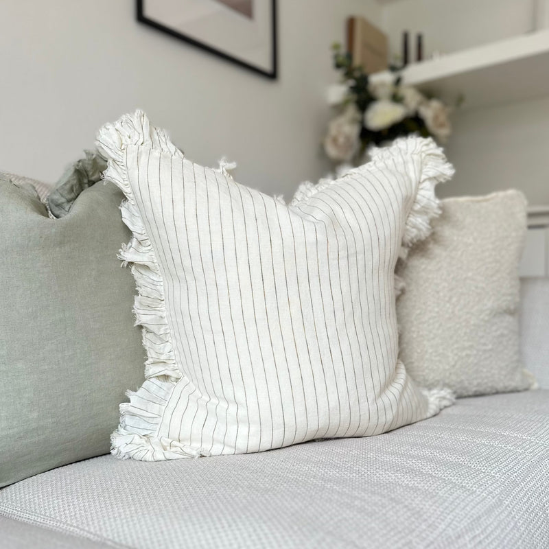 ruffled edge cream square cushion with an olive vertical pin stripe. Sat on a cream sofa.