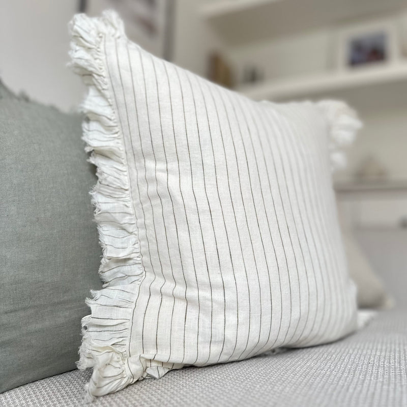 Close up of ruffled edge cream square cushion with an olive vertical pin stripe. Sat on a cream sofa.