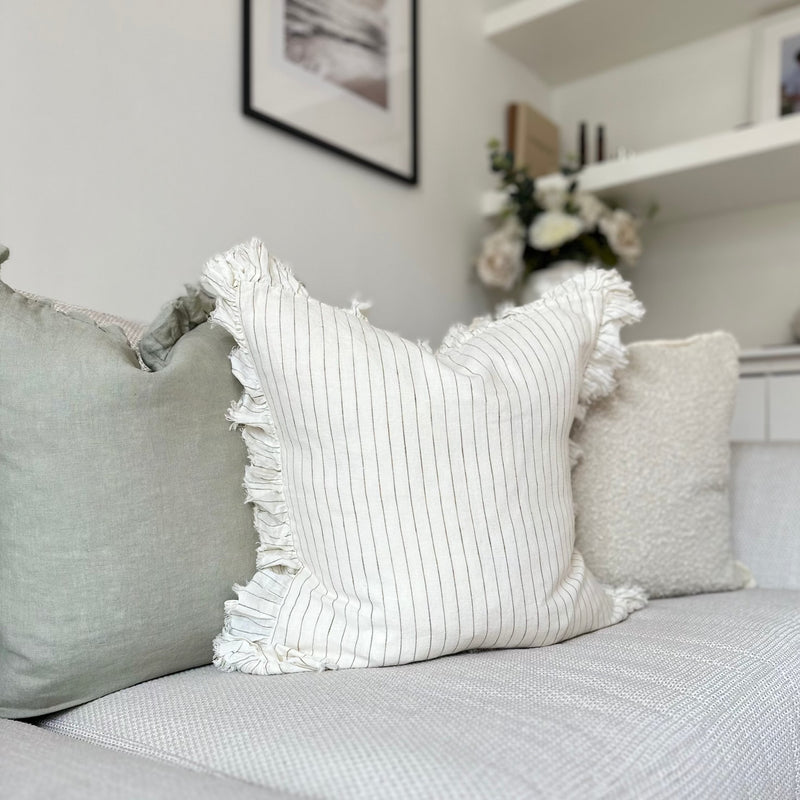 ruffled edge cream square cushion with an olive vertical pin stripe. Sat on a cream sofa.