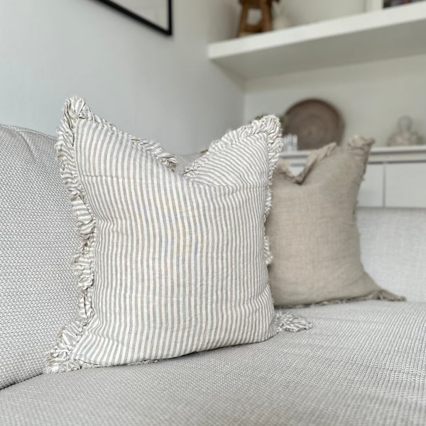 ruffled edge cream cushion with an vertical close repeating beige stripe. Sat on a cream sofa.