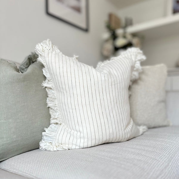 ruffled edge cream square cushion with an olive vertical pin stripe. Sat on a cream sofa.