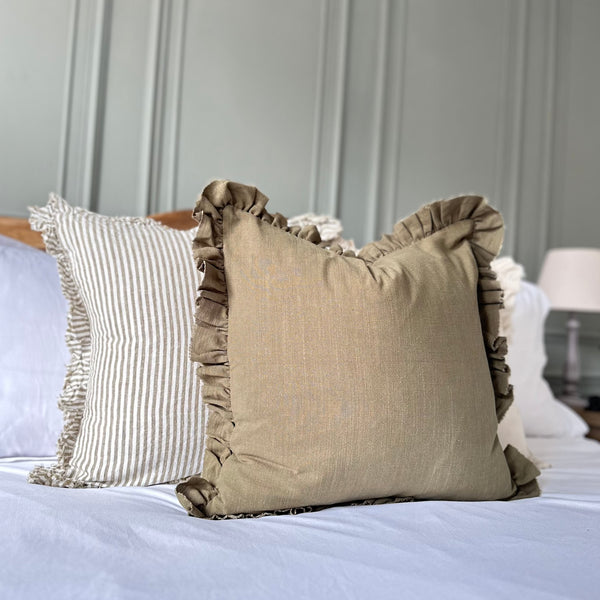 olive green cushion with ruffled edges. Sat on a bed with white bedding.