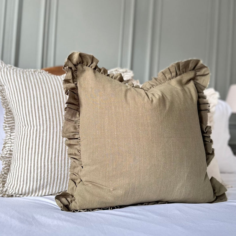 olive green cushion with ruffled edges. Sat on a bed with white bedding.