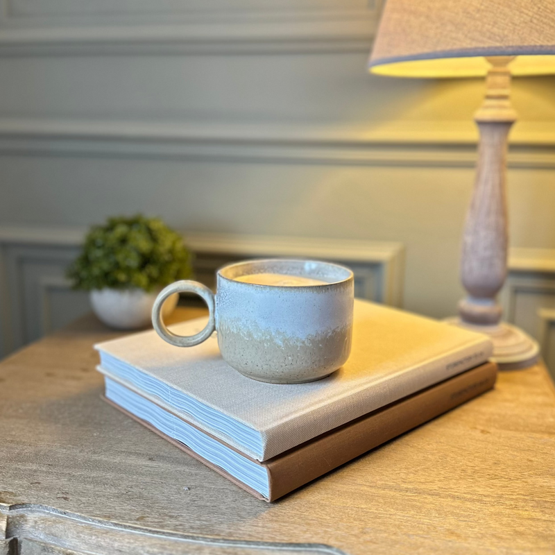 glazed ombre neutral toned round mug with a large circle handle. Sat on a book on top of a wooden bedside table.