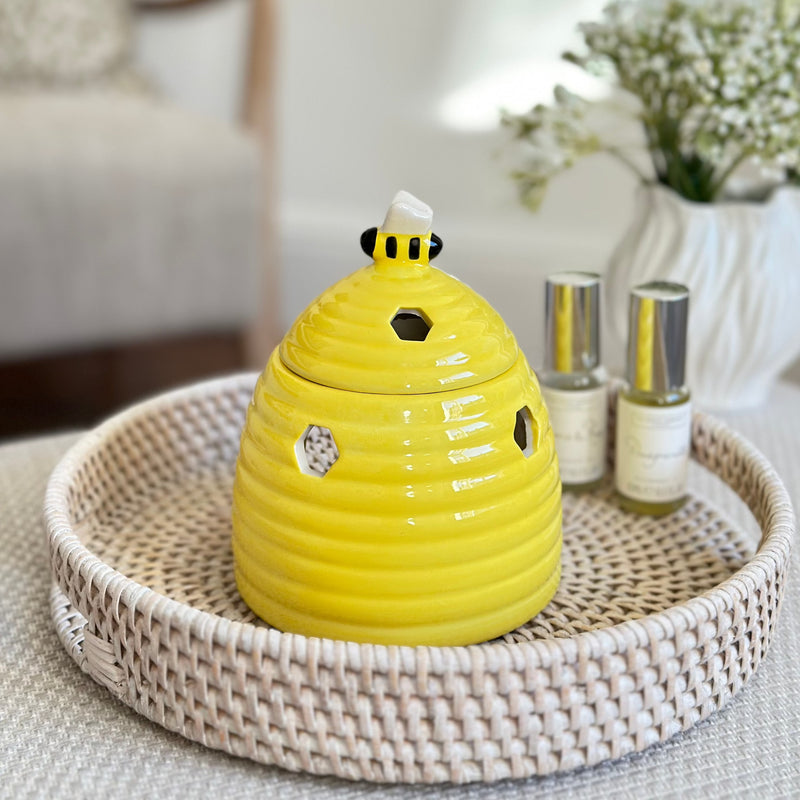 Ceramic yellow beehive shaped oil and wax burner with bumble bee in lid. All sat on a rattan round white tray