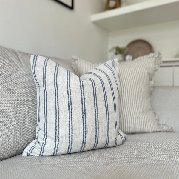 Light cream cushion with navy blue vertical double stripe motif all the way around the cushion. sat on a light cream sofa