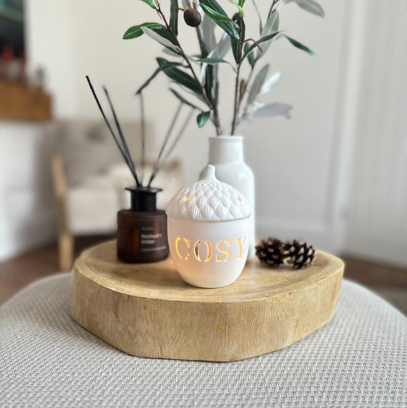 white ceramic tea lguth holder in the shape of an acorn. Sat on a wooden board in a living roon.