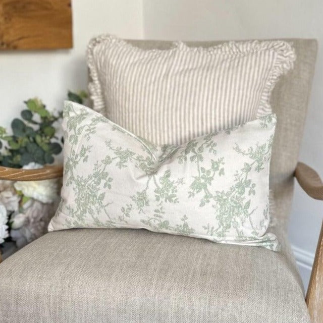 rectangle cream cotton cushion with an all over light green floral pattern. Sat on a cream armchair.