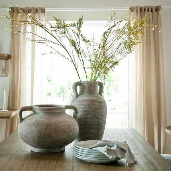 brown ribbed tall slim vase with handles at each side at the top in a greek style. Sat in the centre of a wooden dinging table