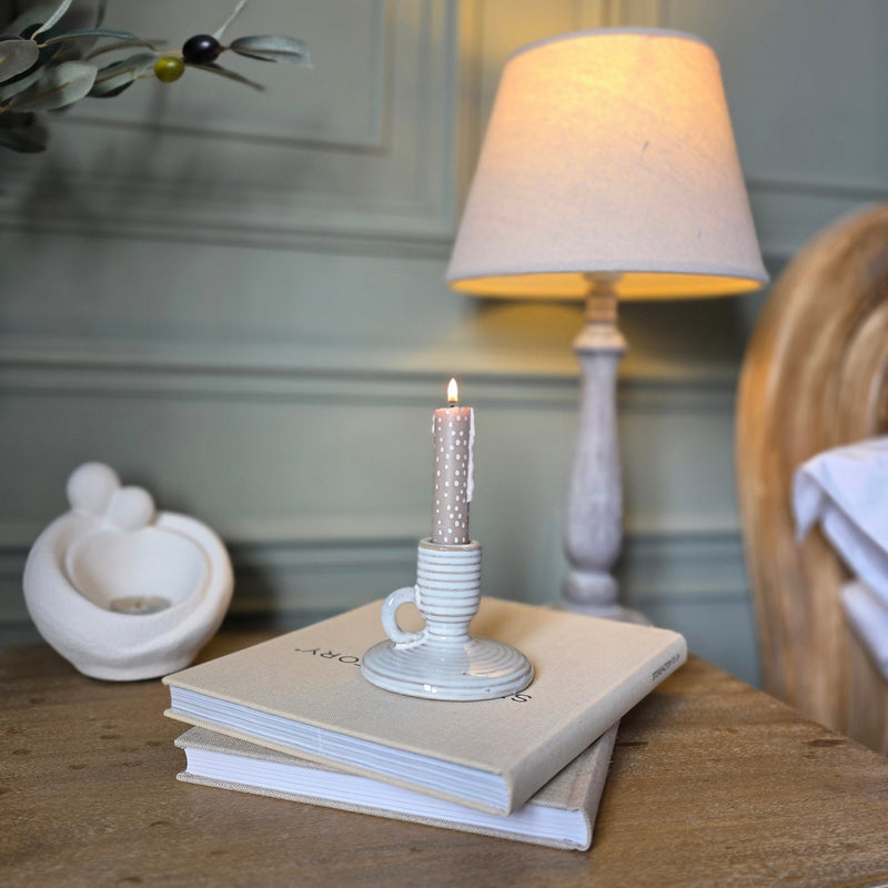 Neutral Ceramic candle holder with handle holding a candle stick sat on a wooden bedside table