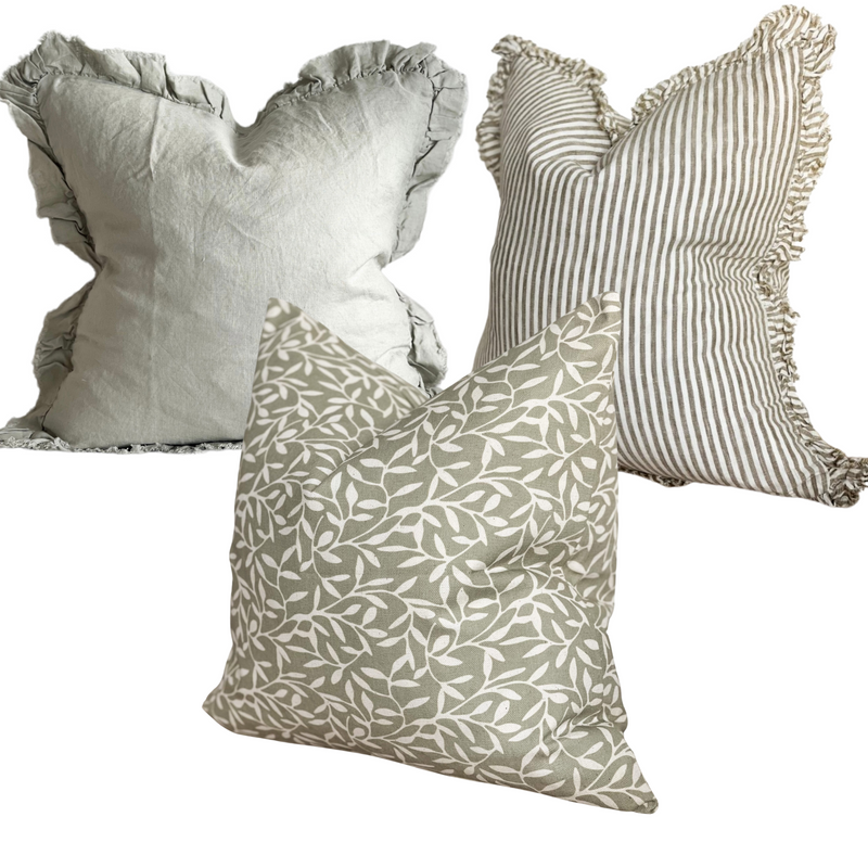 1 square ruffled edge sage green linen cushion, 1 square ruffled edge linen cream and chunky olive green stripes. 1 square cotton olive green cushion with an all over cream olive leaf print. All sat on a plain white background.