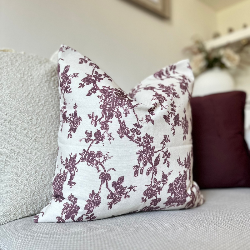 Square cream cushion with an all over plum floral print sat on a cream sofa