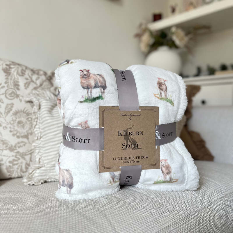 Soft, fluffy white sherpa blanket with an all over white sheep print. Sat on a cream sofa