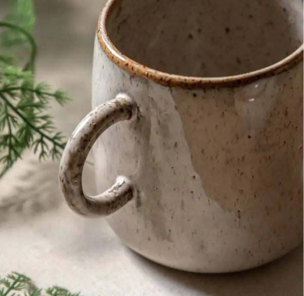 Close up of the speckled glazed mug handle. Beige all over colour mug with a darker brown rim around top of cup and darker speckled rustic style speckles