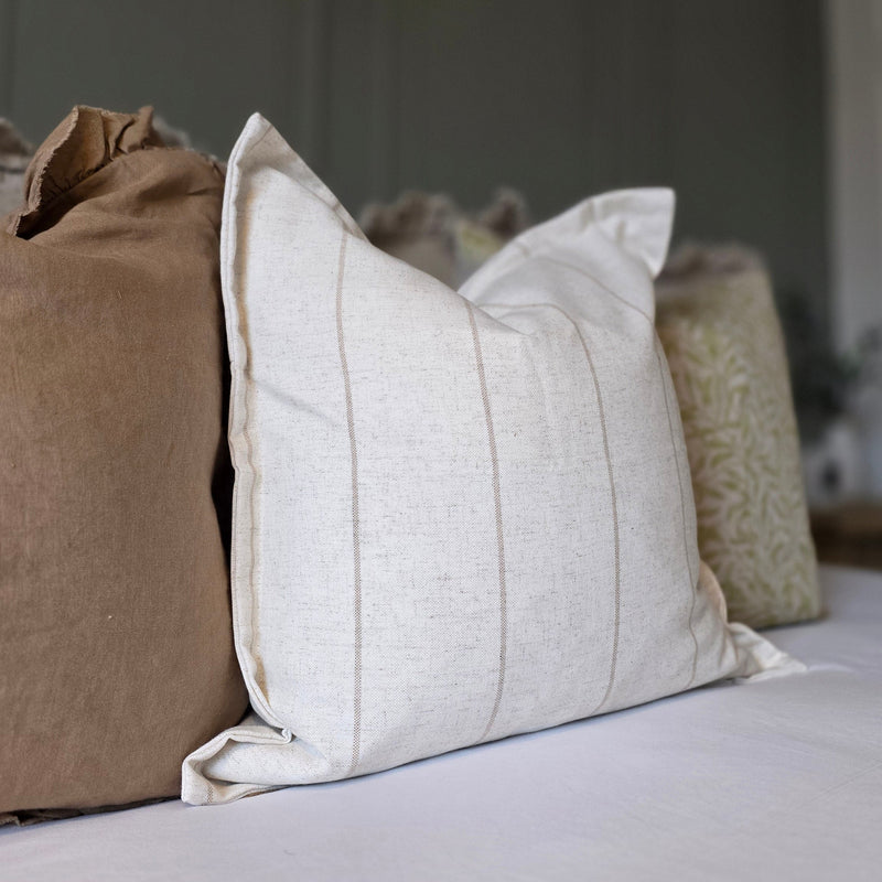 Square flanged edge cotton cream and beige stripe cushion sat on a bed with white bedding