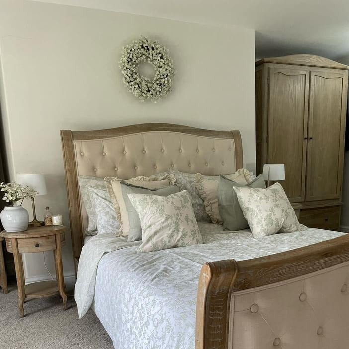 Square linen weathered edge sage green cushion laid with a cream linen cushion and sage floral cushion sitting on a farmhouse style bed
