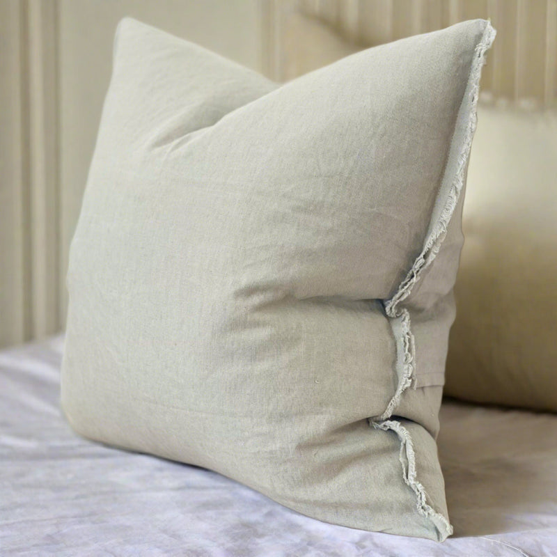 weathered edge square sage green cushion sat on a white bed sheet in a bedroom