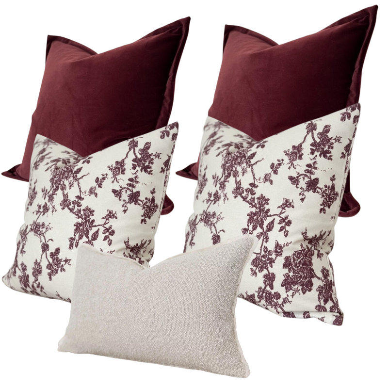 Set of 5 cushions. 2 x square velvet burgundy cushions, 2 x square cream cushions with a burgundy floral print and 1 x rectangle cream boucle cushion. All on a white plain back ground
