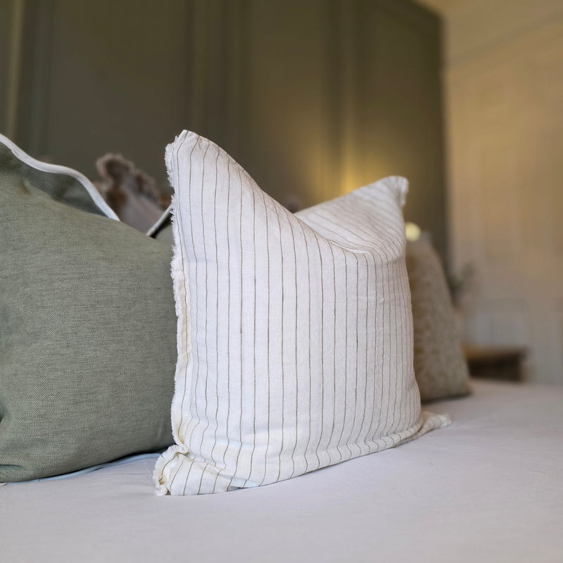 Close up of weathered edge cream square linen cushion with an all over vertical olive pin stripe