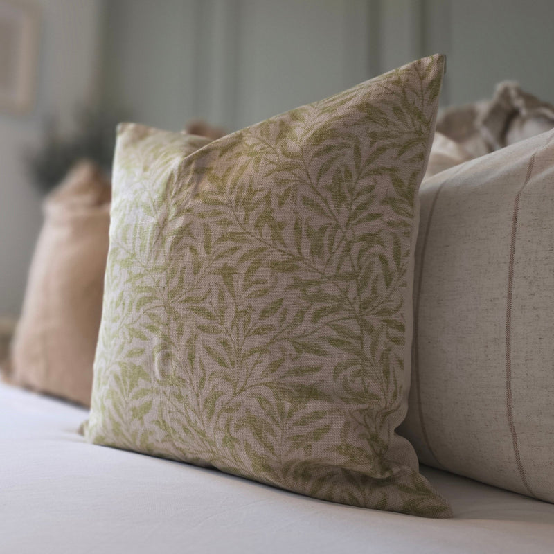 Close up of the beige cushions with an intricate green leaf all over print. Sat on a bed