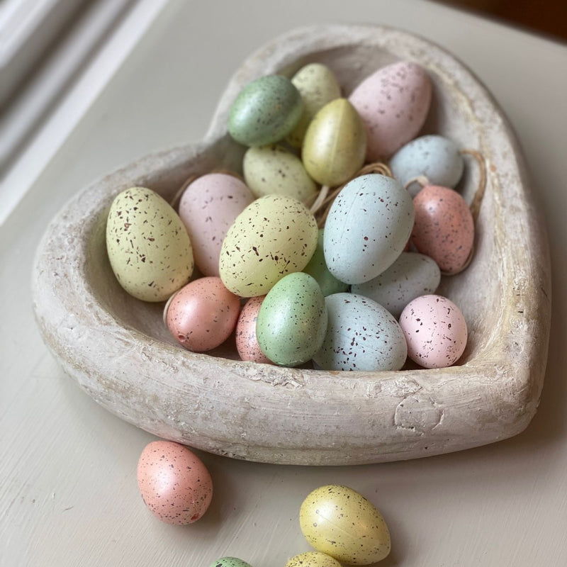 Deep Stone White Heart Dish with decorative small pastel coloured eggs inside. Sat on a wooden bedside table