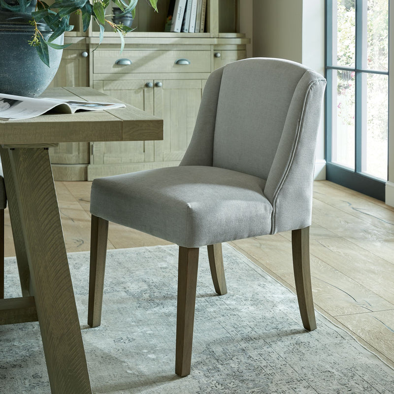 grey fabric dining chair with straight wooden legs. Sat around a rustic wooden dining table.