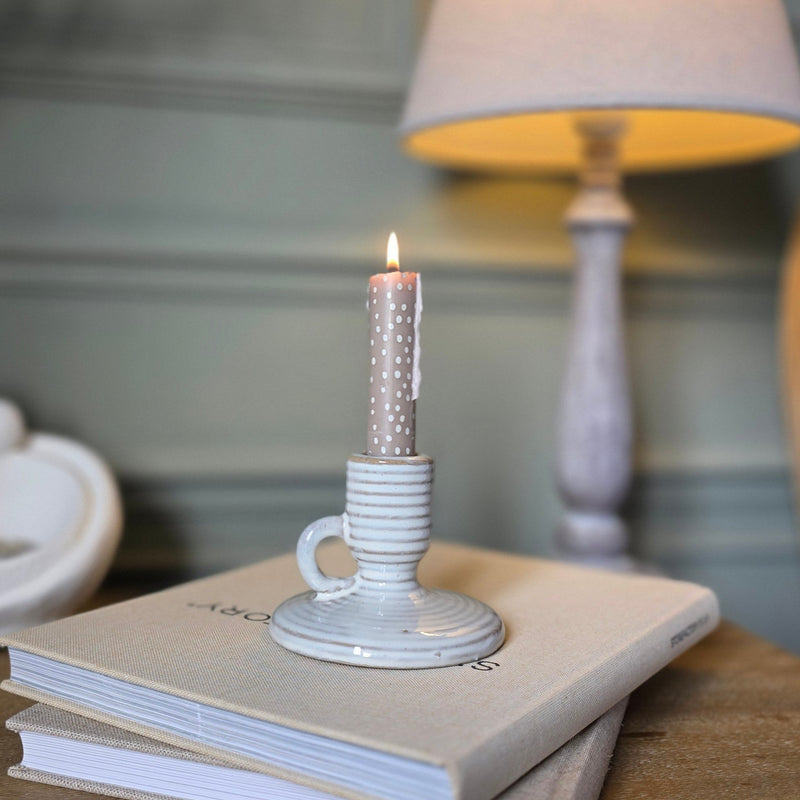 beige stripe small candle holder with handle sat on a beige book on a bedside table