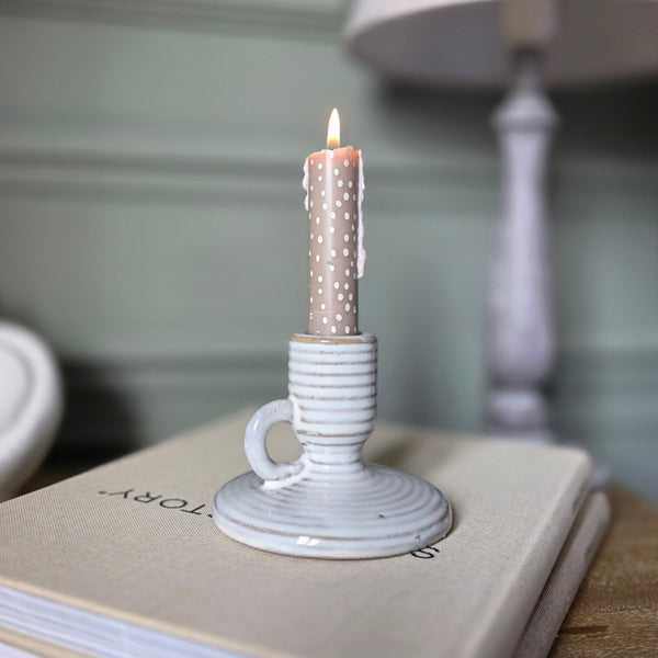 small ceramic neutral stripe candle holder sat on a bedside table holding a lit beige candle stick