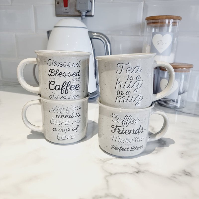 4 ceramic light grey mugs with tea and coffee lover slogans on sat on a white kitchen worktop