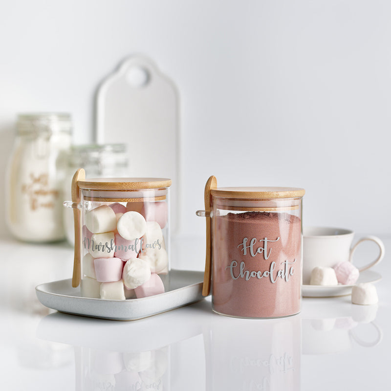 Two glass jars with bamboo lid and spoon with personalised hot chocolate and marshmallows