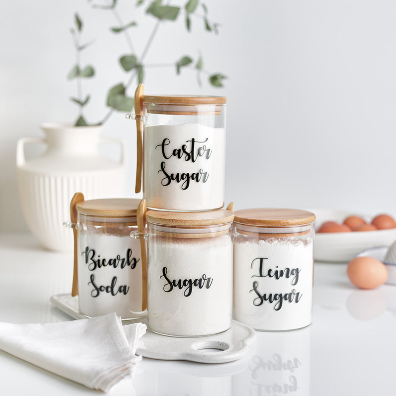 Four glass jars with bamboo lid and spoon with customisable black wording storing bicarb soda sugar icing sugar and caster sugar