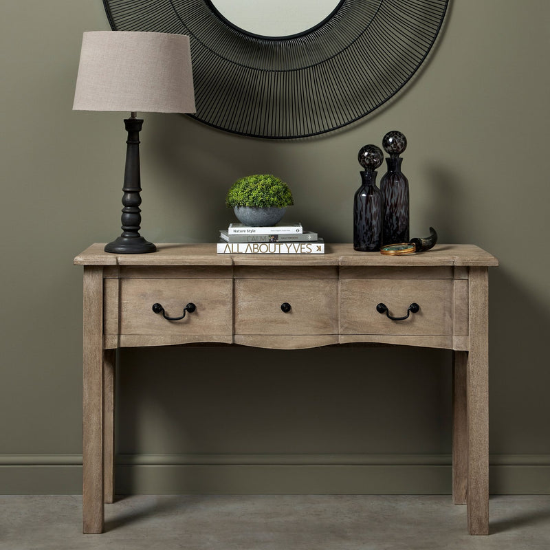 2 drawer wooden console table. With a wood colour. black metal handles. Books and a lamp displayed on the top in a hallway