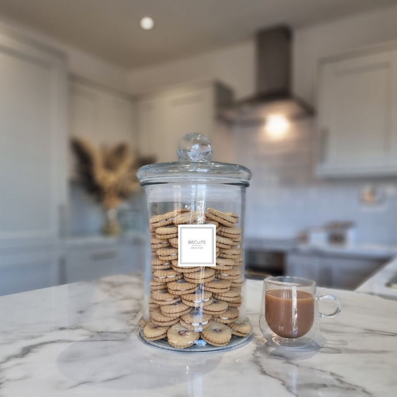 large clear glass jar with square white label central to jar saying "Biscuits" Jar full of biscuits sat on marble kitchen worktop